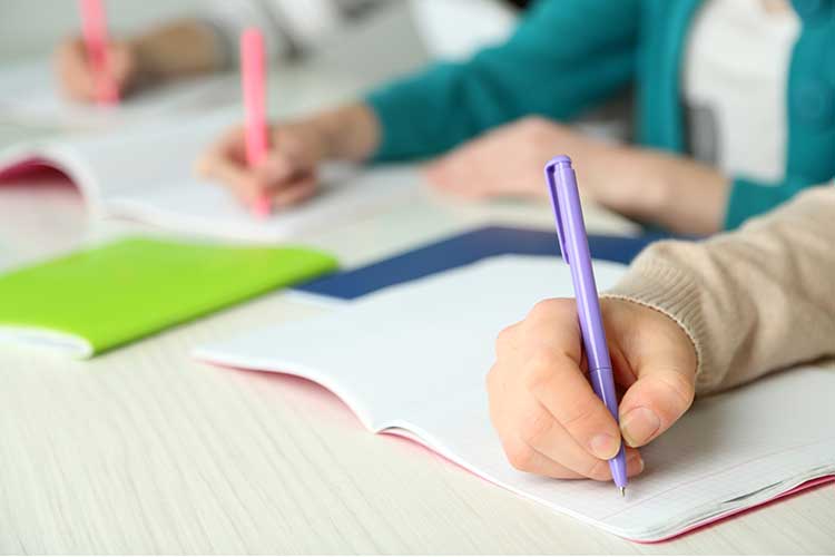 Student writing in a notebook during a classroom assignment